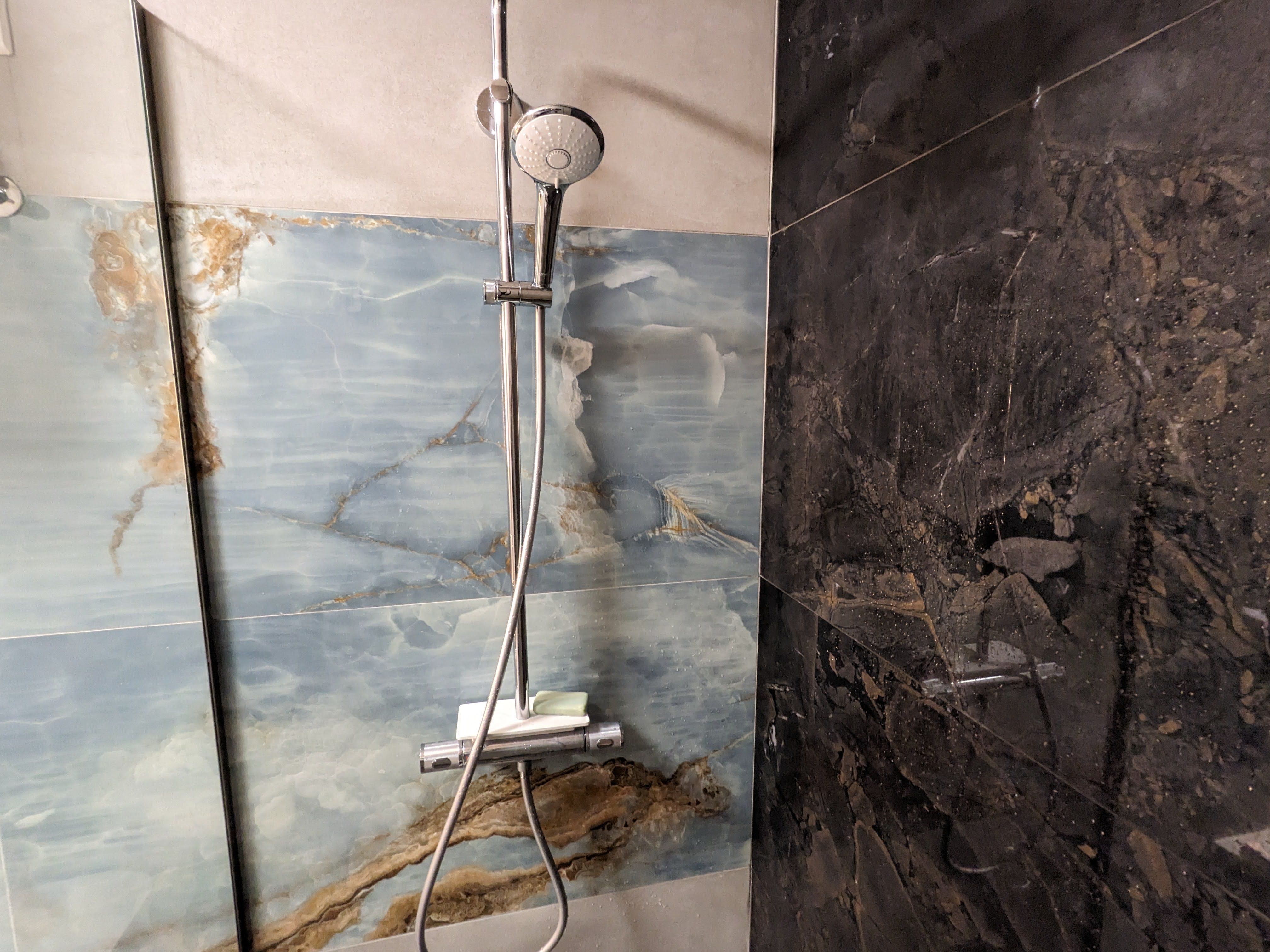 Walk-in shower tiled in blue onyx and dark marble with a rainfall shower head