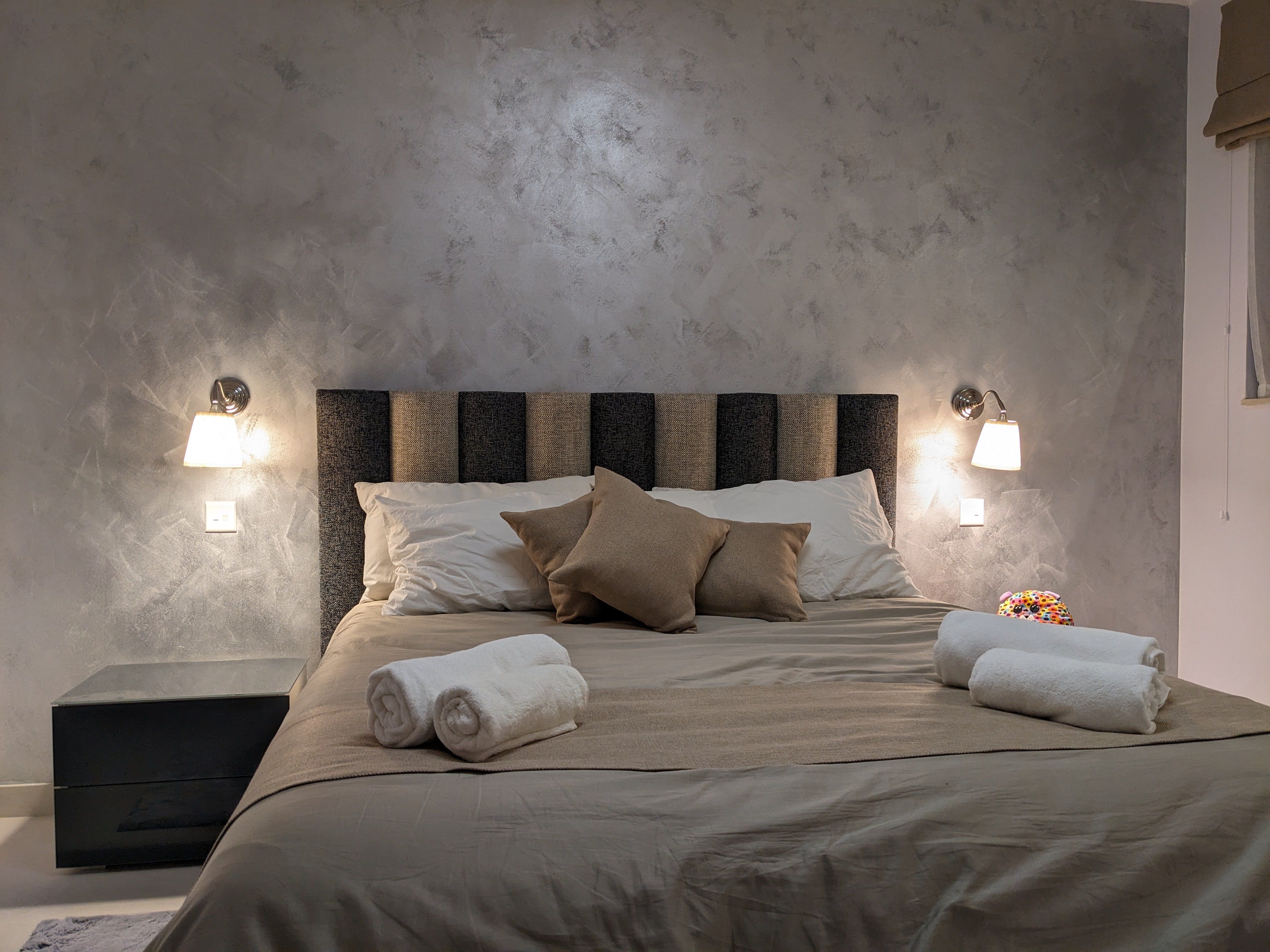 Master bedroom with a panelled headboard, wall reading lights and towels folded on the bed