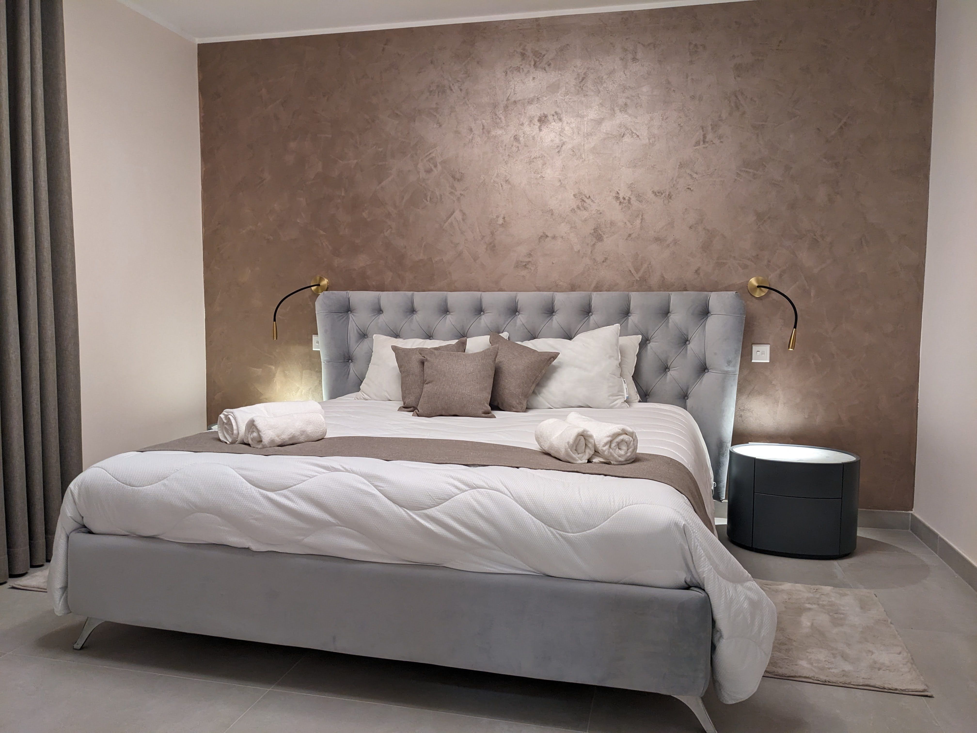 Second bedroom with a buttoned grey headboard and brass reading lights against a bronze wall