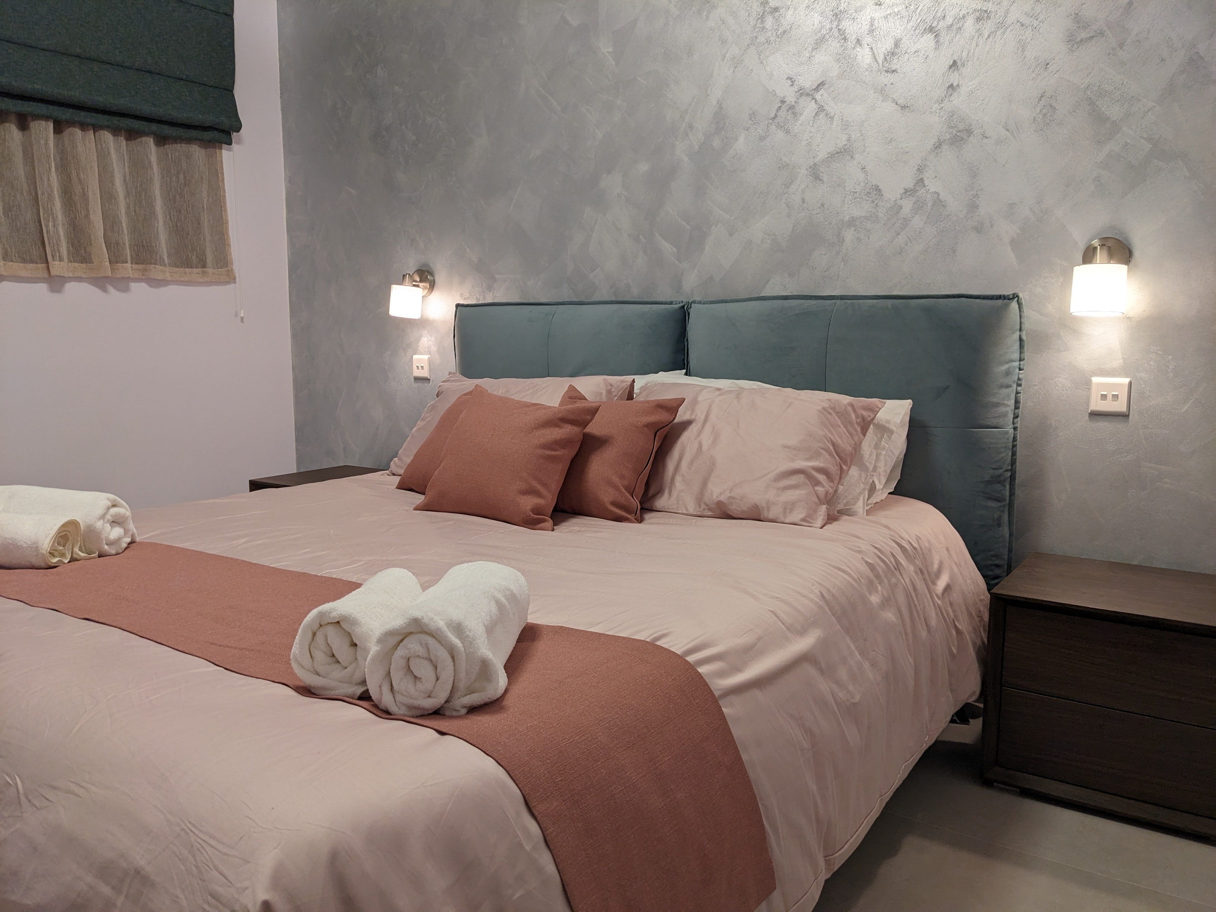 Third bedroom with a teal headboard and terracotta linens, flanked by wall lights