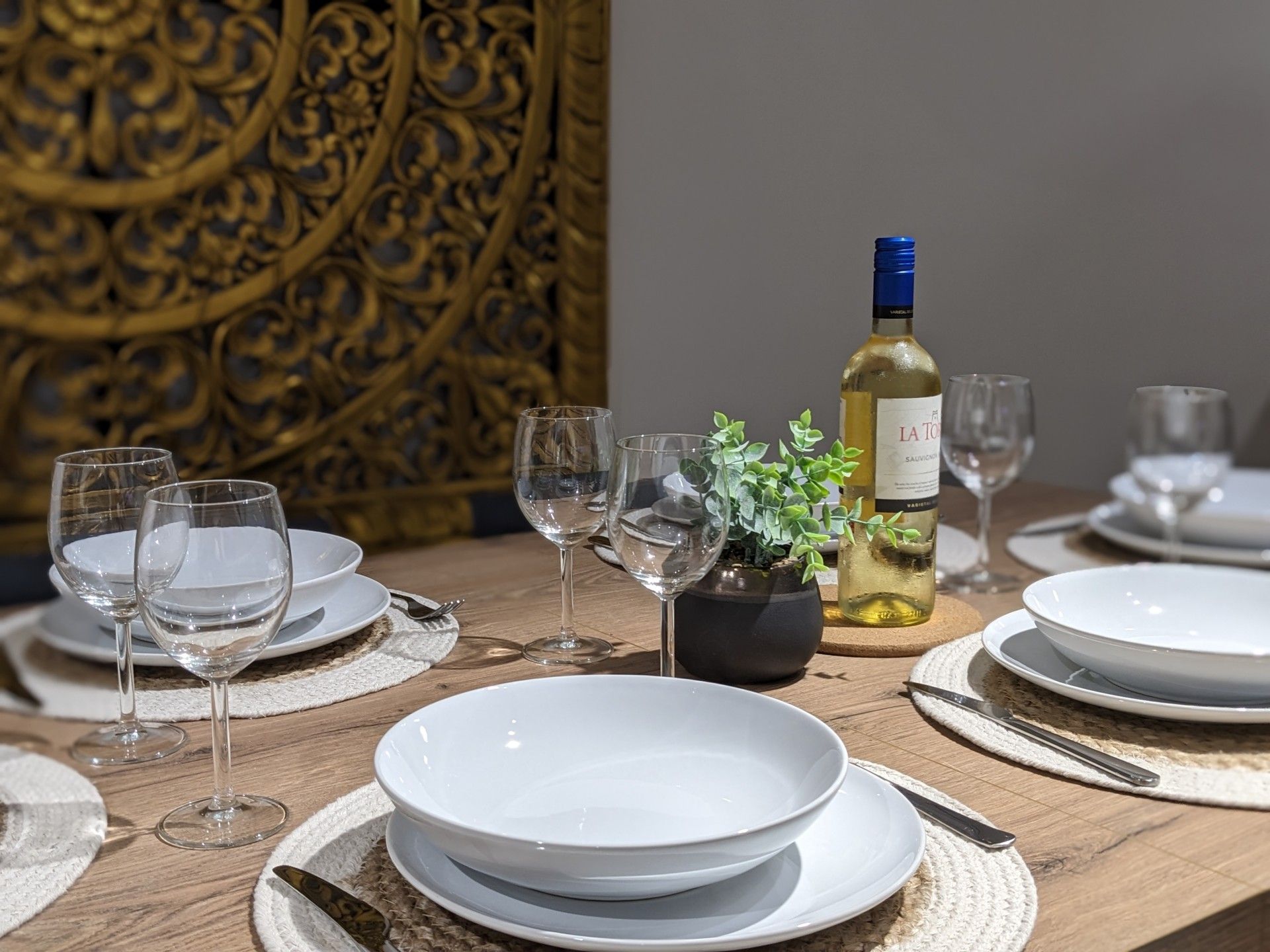 Close-up of the dining table set with wine glasses, white bowls and a bottle of white wine