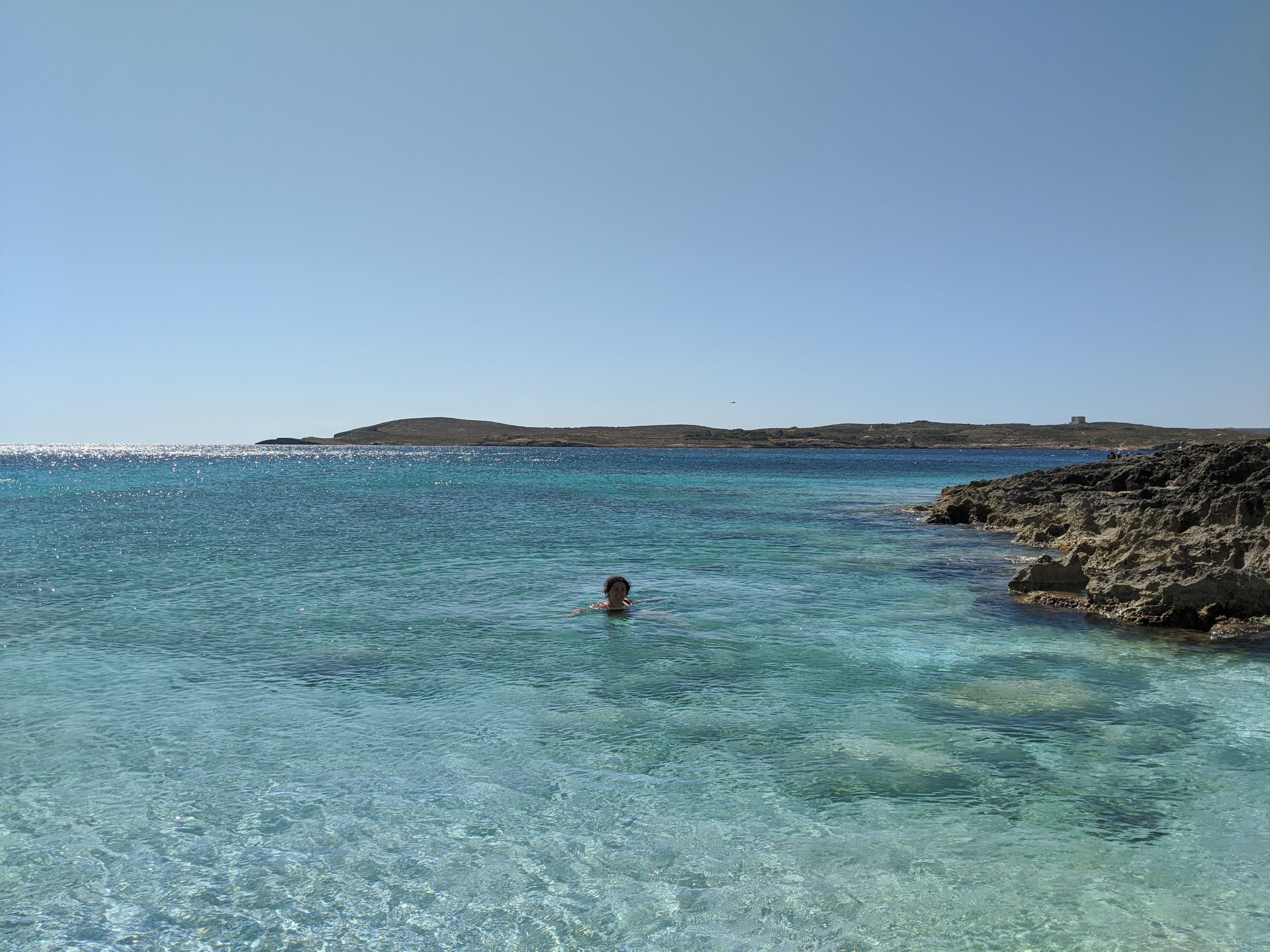The shallow turquoise water at Hondoq ir-Rummien, looking across to Comino, with the limestone shoreline on the right.